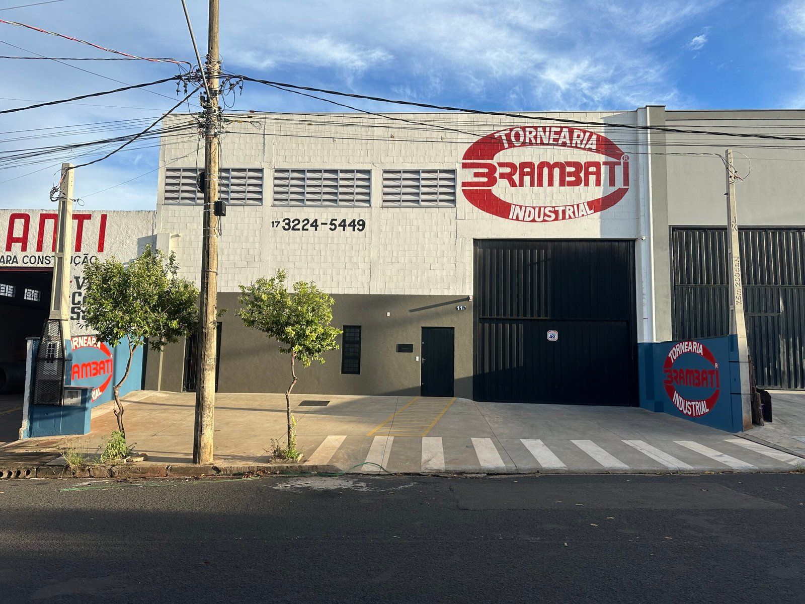 Fachada da Tornearia Brambati, galpão de concreto com o logotipo vermelho pintado na parede e o telefone 17 3224-5449, no Distrito Industrial Adail Vetorazzo.